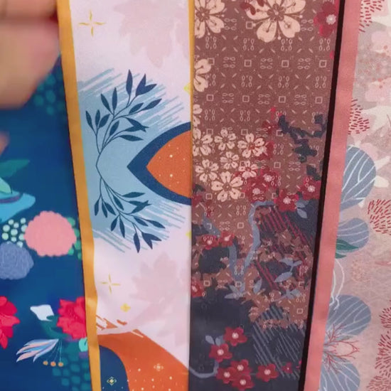Video showcasing a personalized orange and navy blue twilly scarf with abstract botanical patterns, delicate floral details, contrasting borders, and custom Molly lettering on both pointed ends.