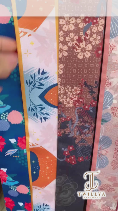 Video showcasing a personalized orange and navy blue twilly scarf with abstract botanical patterns, delicate floral details, contrasting borders, and custom Molly lettering on both pointed ends.