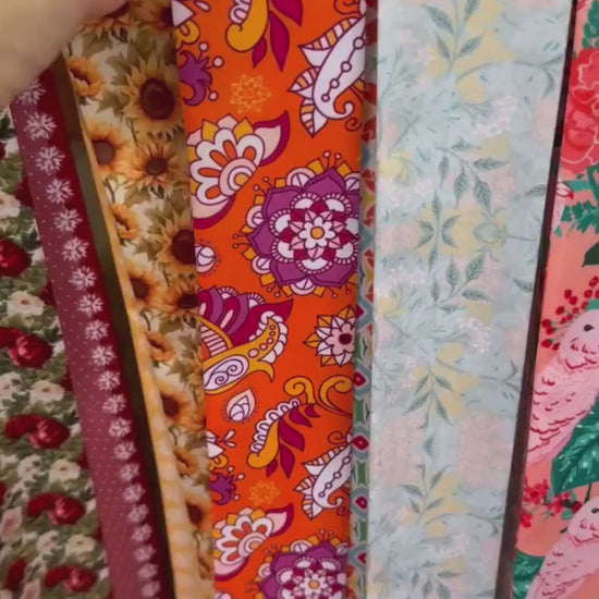 Colorful bohemian twilly scarf showcasing intricate mandala-inspired flowers, orange paisley patterns, and vibrant turquoise geometric details. Finished with personalized name printing on contrasting pink and coral pointed ends, this versatile skinny scarf adds a playful retro touch to handbags, hairstyles, and everyday outfits.
