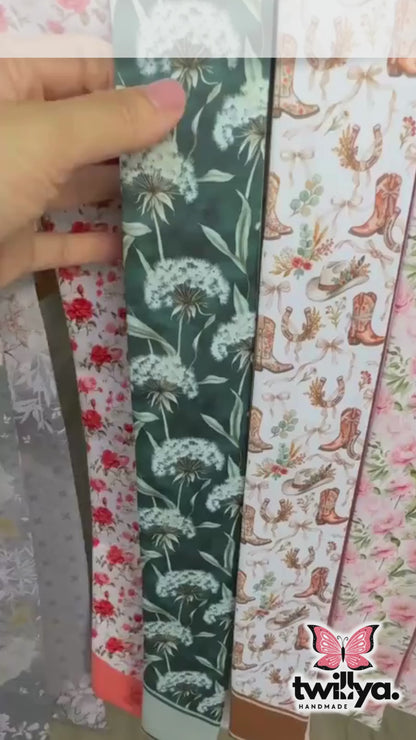 Close-up video of sage green botanical skinny scarf featuring delicate white dandelion illustrations and elegant soft green detailing 