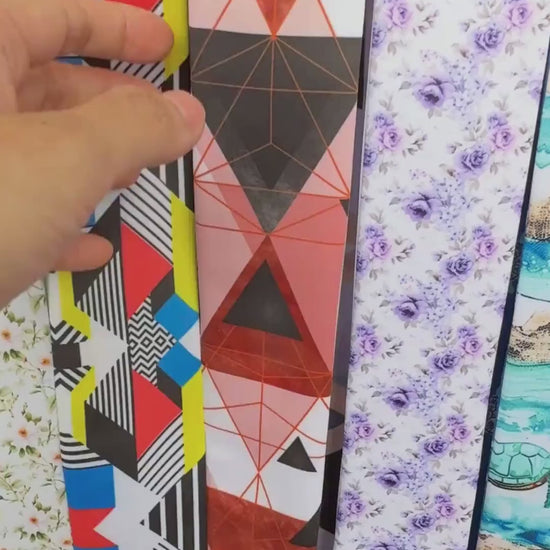 Personalised double-sided satin twilly scarf featuring modern abstract geometric designs with bold triangles, hexagons, and cube-inspired patterns in coral pink, terracotta, slate blue, black, and beige. Both pointed ends display the custom name Julia, creating a stylish accessory for handbags, hair styling, or gifting.