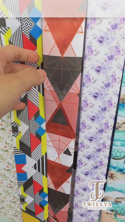 Personalised double-sided satin twilly scarf featuring modern abstract geometric designs with bold triangles, hexagons, and cube-inspired patterns in coral pink, terracotta, slate blue, black, and beige. Both pointed ends display the custom name Julia, creating a stylish accessory for handbags, hair styling, or gifting.