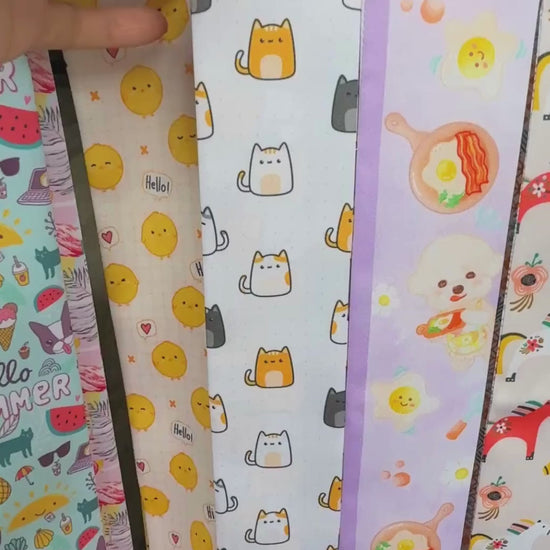 Video showing a playful cat print twilly scarf featuring orange, white and charcoal cartoon cats with contrasting orange and grey details.