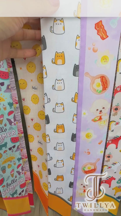 Video showing a playful cat print twilly scarf featuring orange, white and charcoal cartoon cats with contrasting orange and grey details.