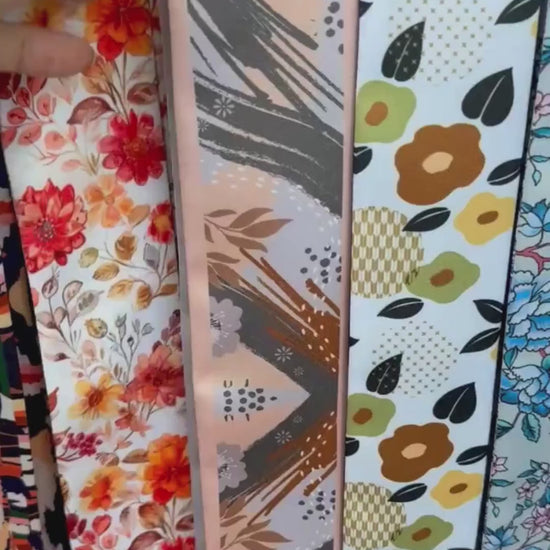 Video showcasing a personalised skinny twilly scarf with abstract botanical patterns, delicate ginkgo leaves, terracotta brushstrokes, and soft peach and charcoal grey tones, highlighting its artistic floral design and custom name detail.