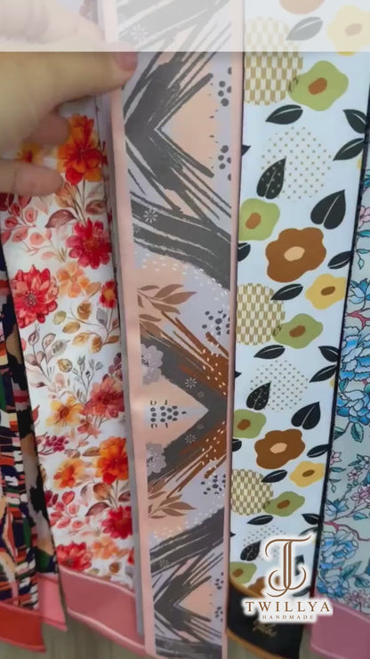 Video showcasing a personalised skinny twilly scarf with abstract botanical patterns, delicate ginkgo leaves, terracotta brushstrokes, and soft peach and charcoal grey tones, highlighting its artistic floral design and custom name detail.
